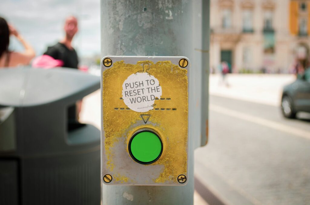 crosswalk button with sticker above it saying "push to reset the world"